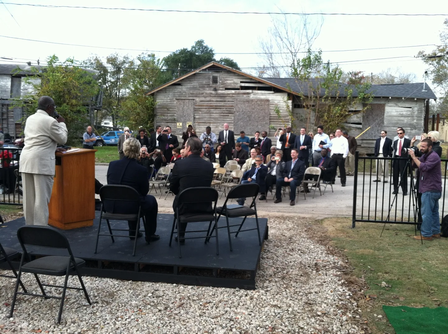 An outdoor neighborhood gathering with speakers, residents, and attendees.